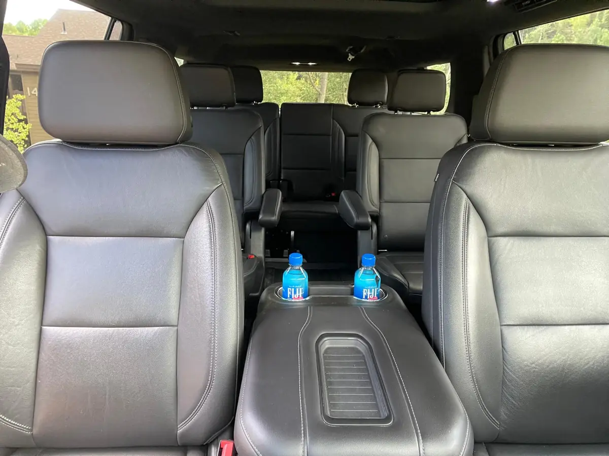 Interior of the black SUV seen from between the front seats, with bottled water in the console, two leather captain's chairs in the second row and a bench seat across the third row