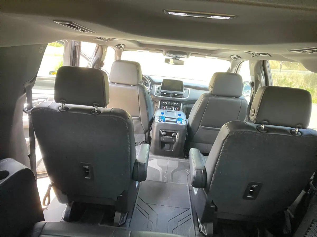 View from the third row bench seat of the SUV looking forward, showing the rear climate control panel on the back of the front console and the aisle between the second row chairs